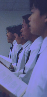 Young men in white shirts and ties singing side by side, holding sheet music